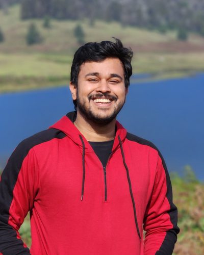 Anchit Gupta, smiling, outdoors in front of a lake